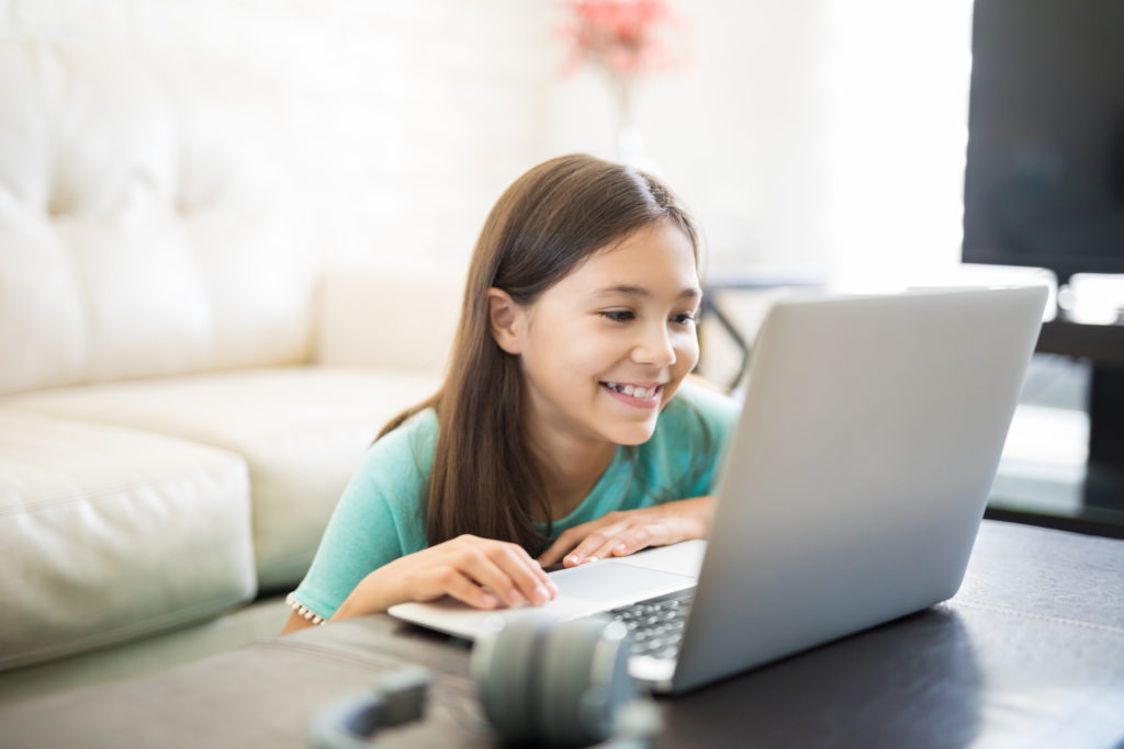 微笑的小女孩在家里客厅的笔记本电脑上使用在线辅导服务
